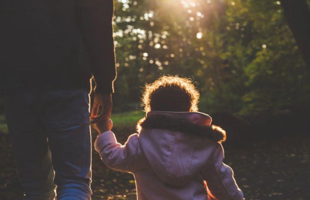 young girl holding father's hand backlit from sun