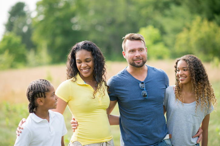 A happy family of four stands together in a sunny field, smiling and enjoying their time outdoors A happy family of four stands together in a sunny field, smiling and enjoying their time outdoors