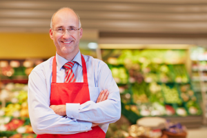 The owner of a supermarket smiling in front of a produce display. The owner of a supermarket smiling in front of a produce display.